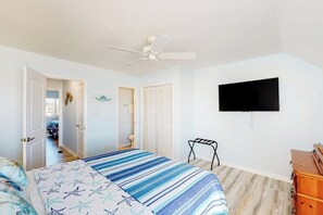 Ein Schlafzimmer mit einem Bett, einem Deckenventilator, einem an der Wand montierten Fernseher und einer Holzkommode.