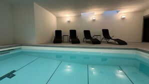 Une piscine entourée de chaises longues et d’une petite table, le tout bordé de murs sobres et éclairé par des spots encastrés.