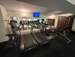 Ein Fitnessstudio mit Laufbändern, Gymbällen und einem Fernsehbildschirm.