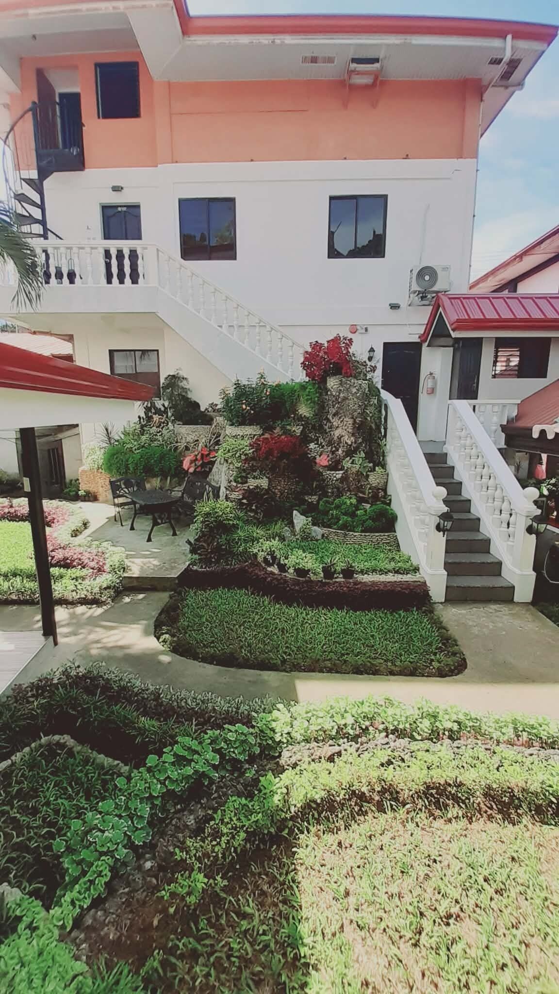 A multi-story building with a central staircase, a small outdoor seating area, and a landscaped garden with various plants.