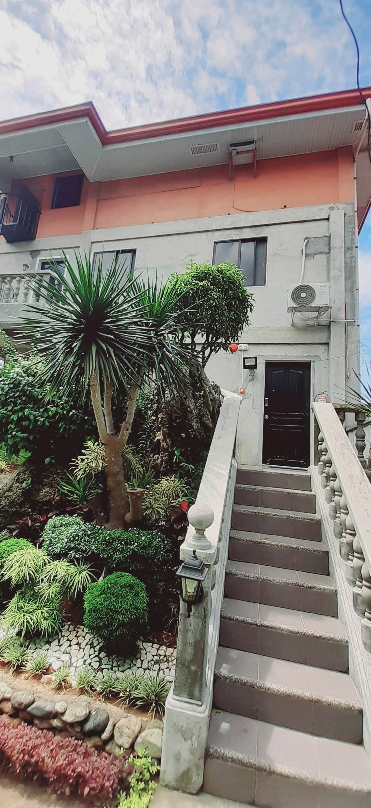 A building with a staircase leading to a door, surrounded by various plants and a small garden area.