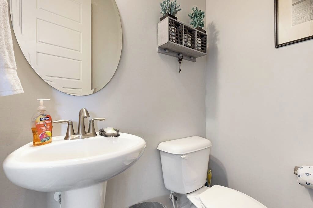 A bathroom with a white sink, toilet, and a wall-mounted shelf with decorative items.
