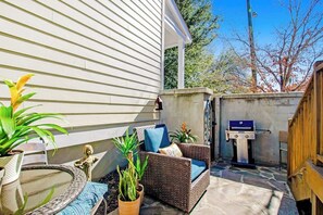 A patio area with a wicker sofa, a round table, and a barbecue grill. - Bright & beautiful home with a darling patio, WiFi, central A/C, & gas grill (Savannah)