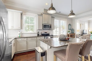 A kitchen with white cabinets, a stainless steel refrigerator, a microwave, and a granite countertop island with chairs. - Bright & beautiful home with a darling patio, WiFi, central A/C, & gas grill (Savannah)