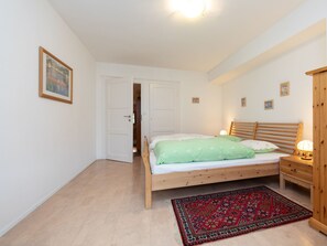 Ein Schlafzimmer mit einem hölzernen Bett, einem Nachttisch, einer Lampe, einer Tür und einem gemusterten Teppich.