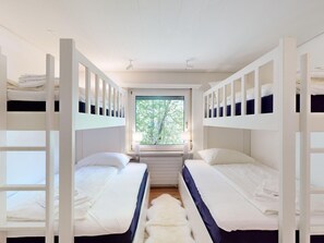 Een kamer met stapelbedden, een raam met uitzicht op bomen, en een witte bonttapijt op de vloer.