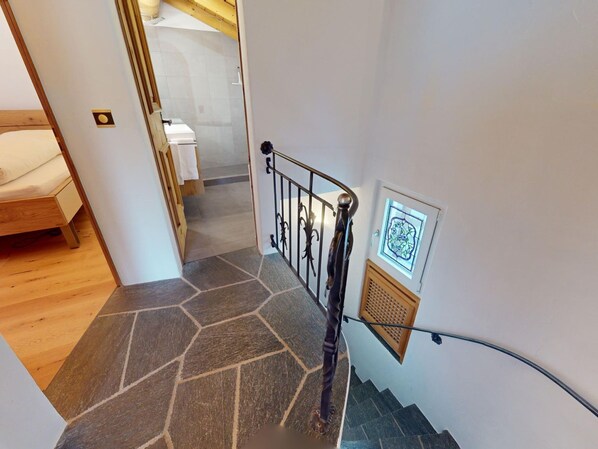 Una escala amb paviment de pedra i barana metàl·lica que porta a una habitació amb llit de fusta i paret blanca.