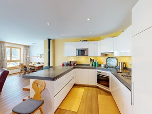 A modern kitchen with white cabinets, a microwave, and a dishwasher. There is a dining area with a wooden table and chairs. - Apartment Macun by Interhome (Silvaplana-Surlej)