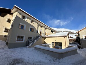 A multi-story building with a snow-covered ground, a staircase leading to the entrance, and a mountain in the background.