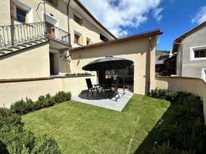 A patio with a table and chairs, a large umbrella, and a well-maintained lawn.
