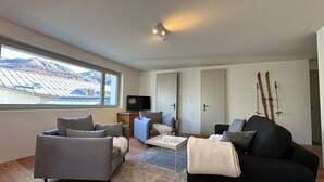 Een moderne woonkamer met een groot raam, een flatscreen televisie en een ski-rek.