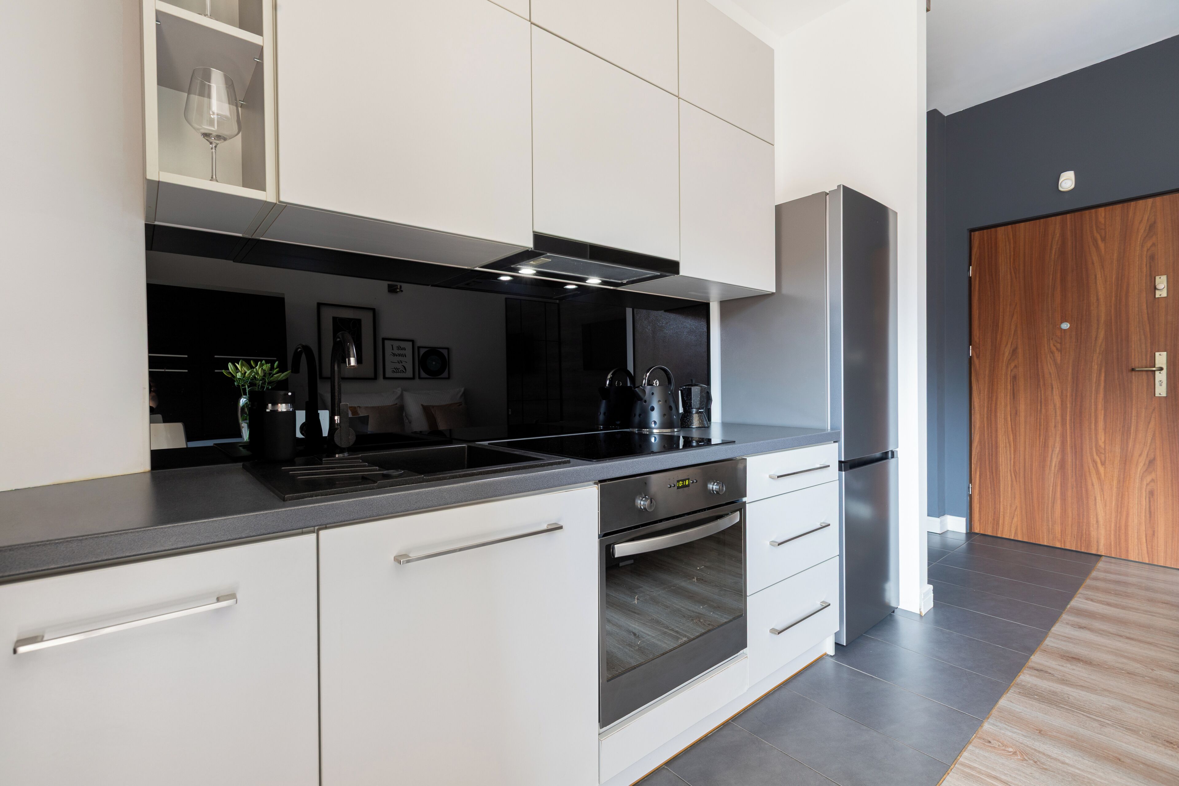 Una cocina moderna con armarios blancos, encimera negra y electrodomésticos de acero inoxidable.