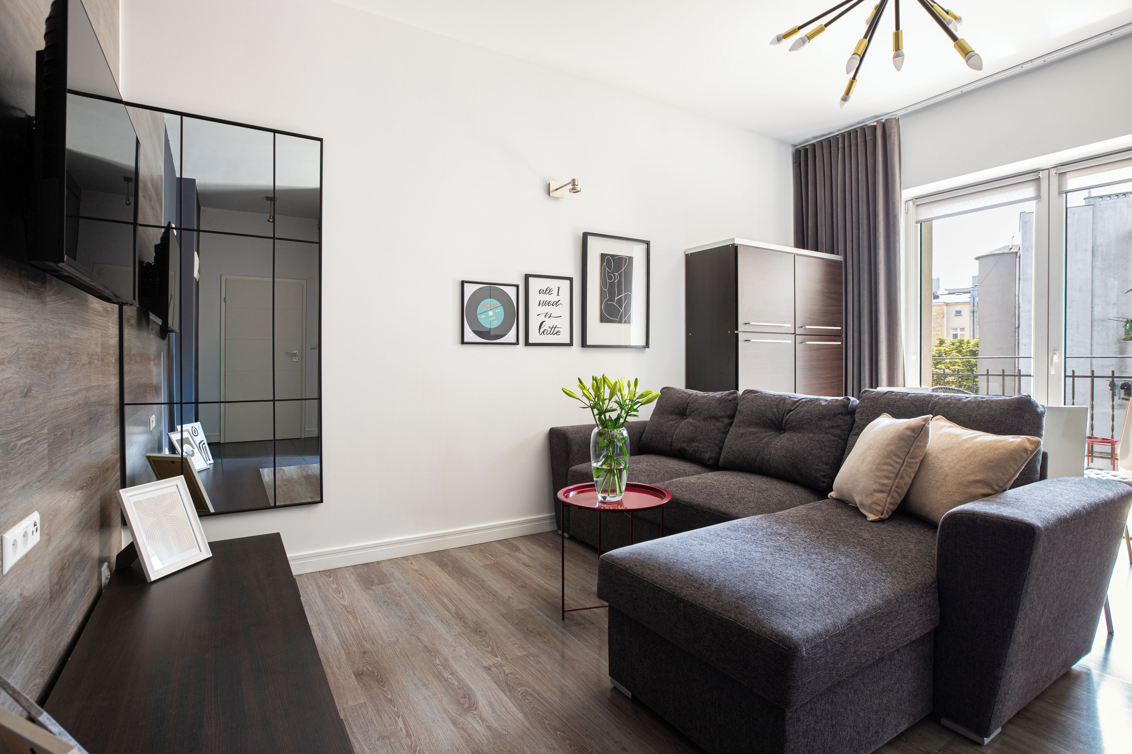Una sala de estar moderna con un sofá modular, un televisor de pantalla plana montado en la pared y un ventanal con cortinas.
