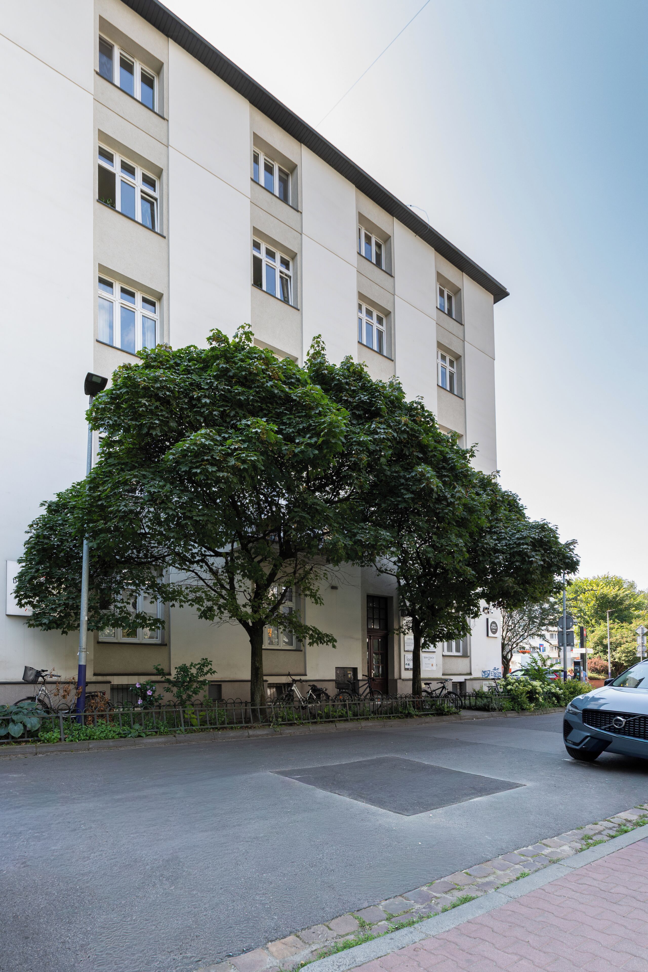 Un edificio de varios pisos con fachada plana, ventanas amplias y un árbol en la parte delantera.