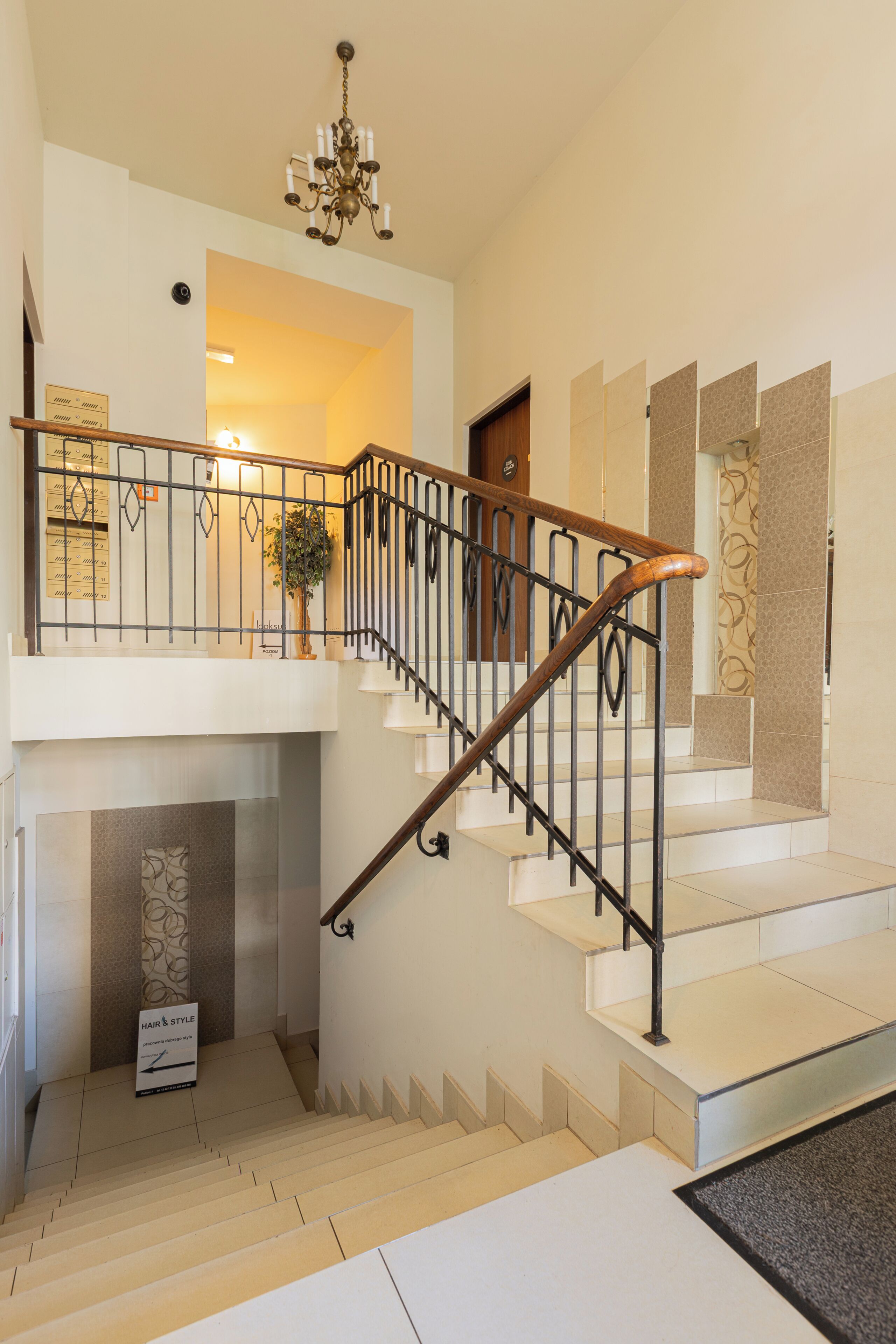 Una escalera con barandilla de madera y balaustradas de metal, que conduce a un rellano con una planta en maceta y un letrero.