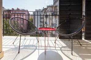 Ein Balkon mit zwei schwarzen Stuhlgestellen aus Draht und einem kleinen roten Tisch.