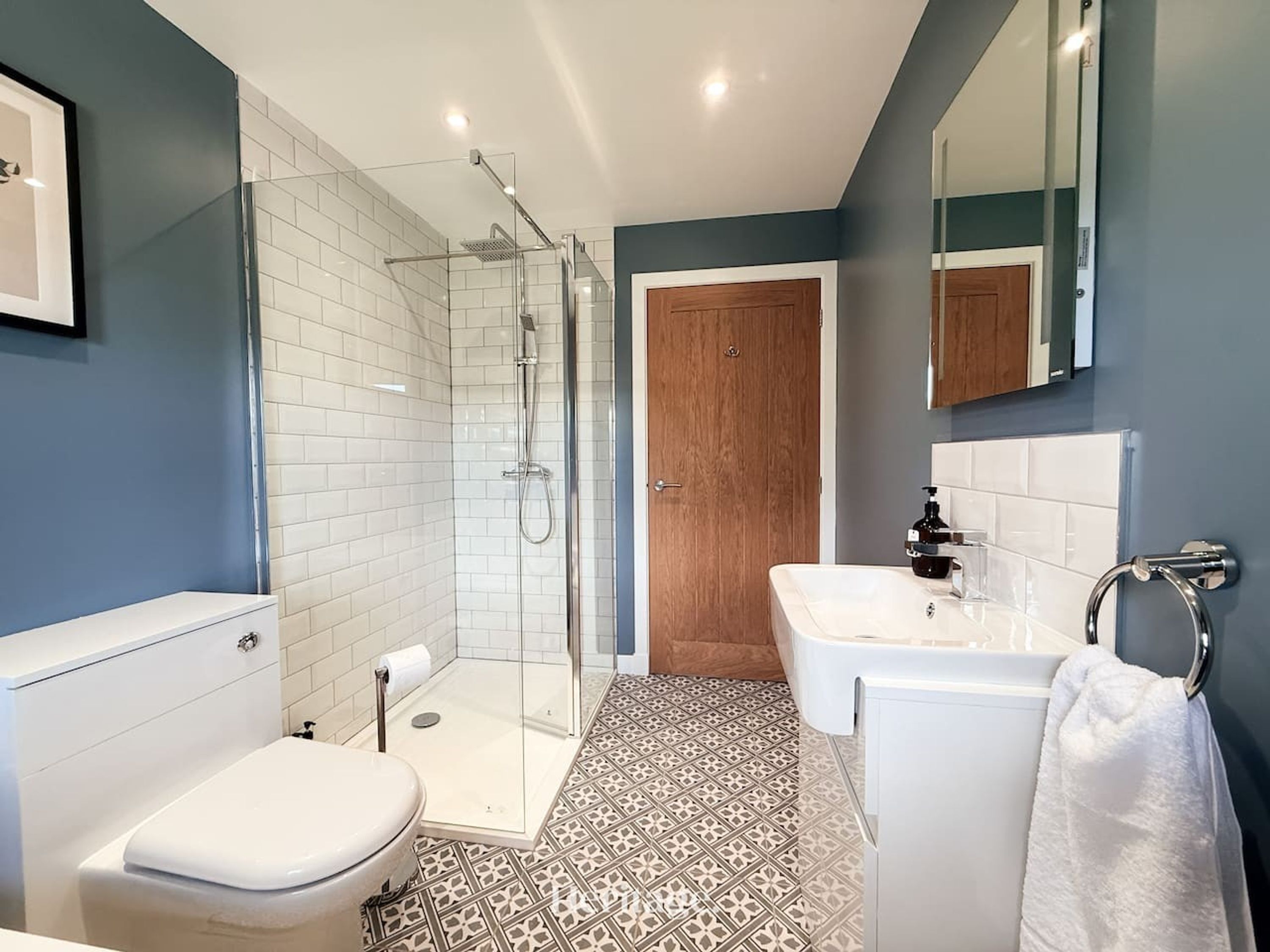 A modern bathroom with a glass-enclosed shower, a white toilet, a sink with a towel ring, and a wooden door.