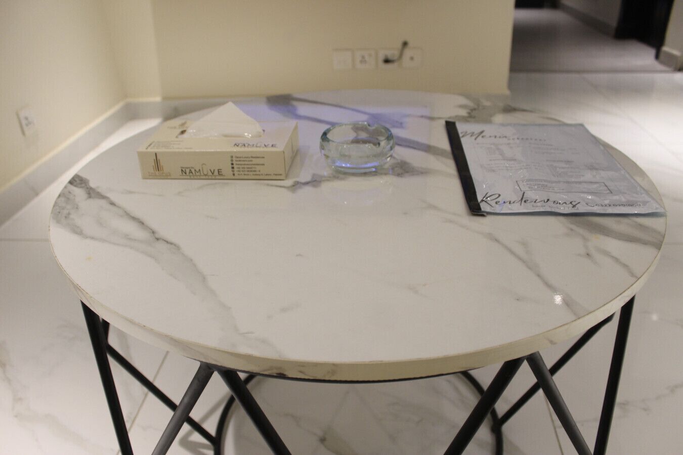 Una mesa redonda de mármol con una caja etiquetada 'NAMUVE' y un menú encima.