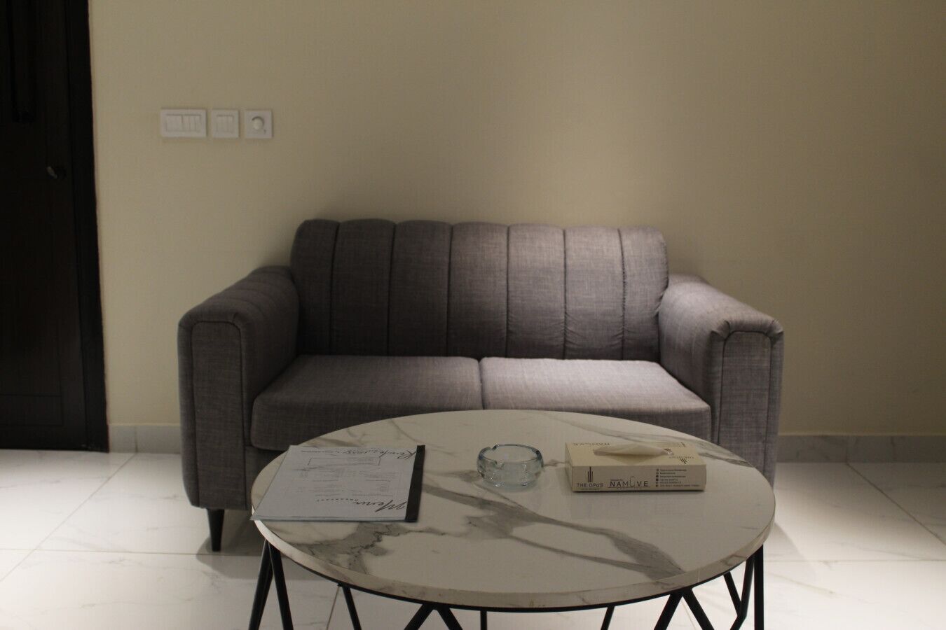 A room with a grey sofa, a round marble table, and a door with a dark frame.