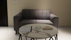 A room with a grey sofa, a round marble table, and a door with a dark frame. - Studio Apt | Roof Garden | The Opus (Lahore)