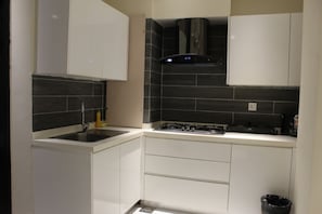 Een kleine keuken met witte kastjes, een zwarte tegel achterwand, een roestvrijstalen spoelbak en een gasfornuis.