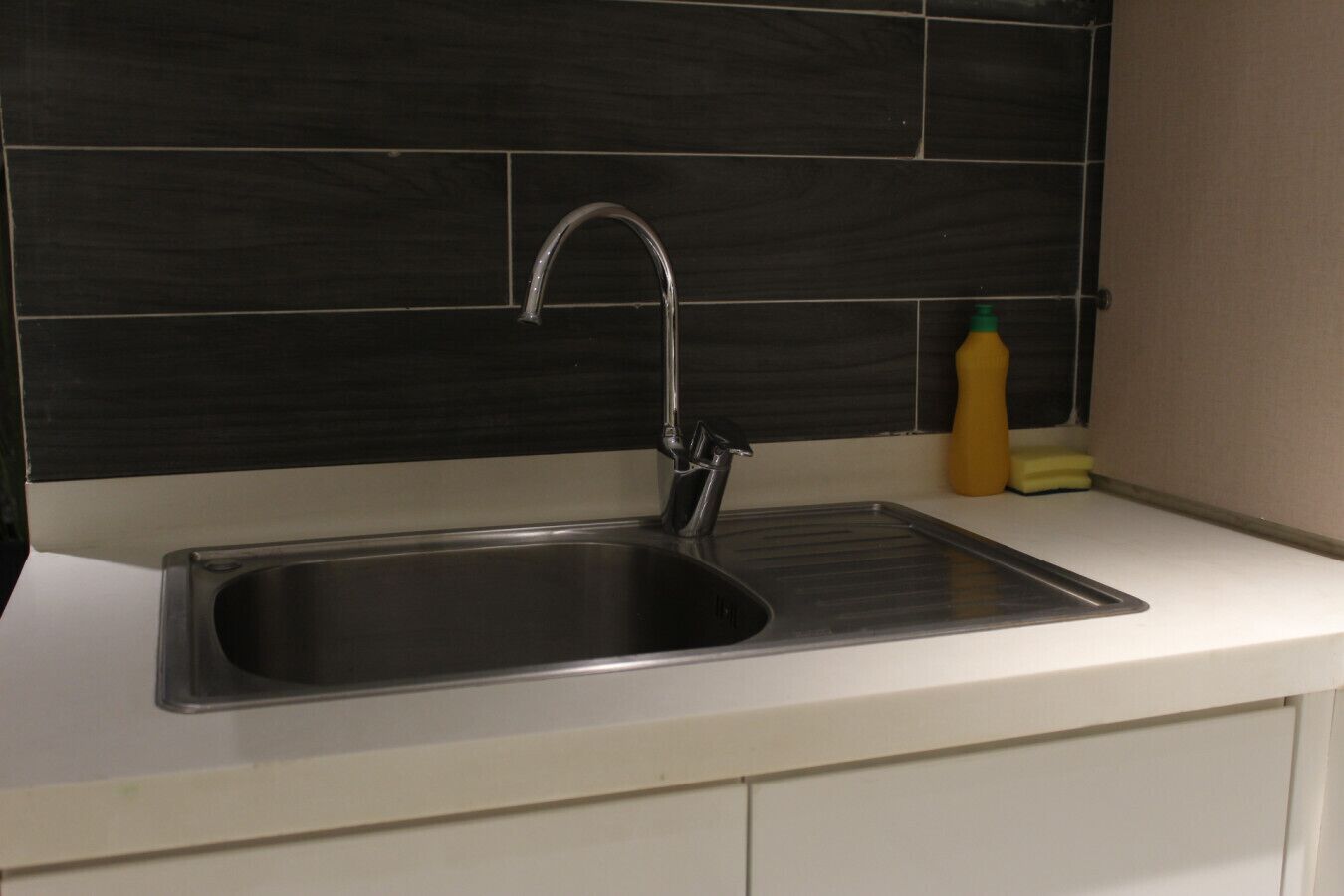 A kitchen with a stainless steel sink, a modern faucet, and a black tiled backsplash.
