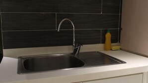 A kitchen with a stainless steel sink, a modern faucet, and a black tiled backsplash. - Studio Apt | Roof Garden | The Opus (Lahore)
