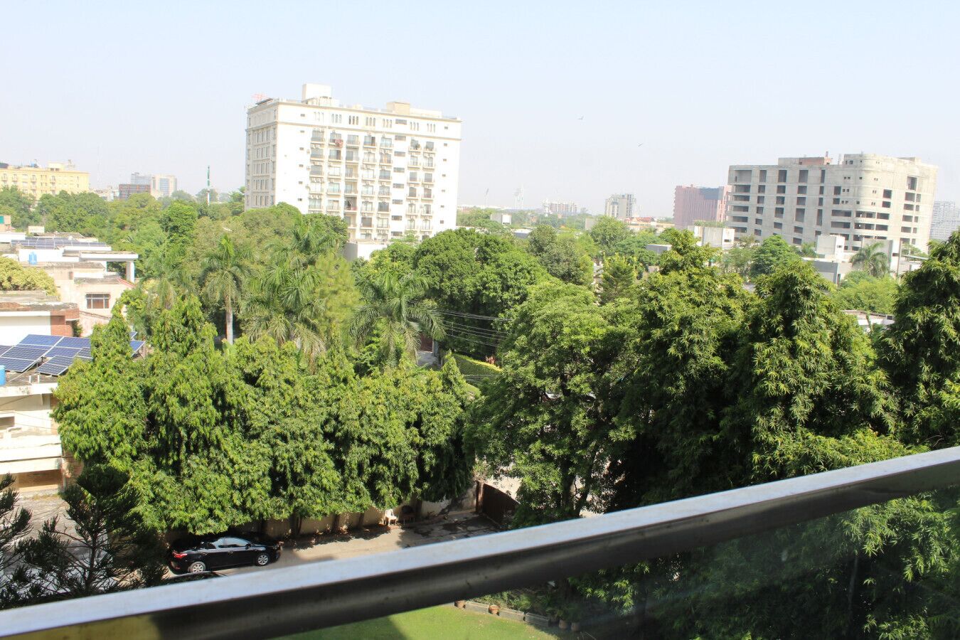 A residential area with multi-story buildings, dense greenery, and a clear sky.