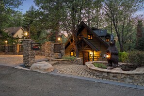 A lodge with a stone entrance, a bear statue, and a well-lit front door. - Disney Imagineer-Built Chalet Near the slopes | Fire Pit, Trails | Hot Tub (Big Bear Lake)