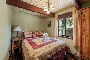 Ein Schlafzimmer mit Holzboden, einem Bett mit einer Steppdecke, einem Nachttisch mit Lampe und einem Fenster mit Vorhängen.