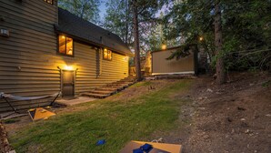 A house with a wooden exterior, a front door, and a staircase leading to a deck. - Disney Imagineer-Built Cabin, Pet Friendly, Fire Pit, Walk to Town Trails (Big Bear Lake)