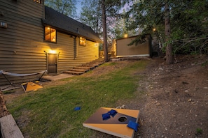 A house with a wooden exterior, a front door, and a staircase leading to a deck. - Disney Imagineer-Built Cabin | Pet Friendly | Fire Pit | Walk to Town Trails (Big Bear Lake)