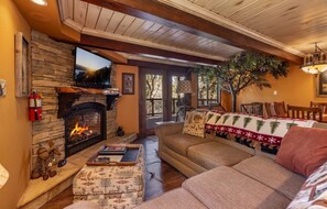 Ein gemütliches Wohnzimmer mit einem Kamin aus Stein, einem bequemen Sofa und einem Fernseher, der über dem Kamin angebracht ist.