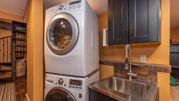 A compact laundry area with a stacked washer and dryer, a stainless steel sink, and dark cabinetry. - Disney Imagineer-Built Cabin, Pet Friendly, Fire Pit, Walk to Town Trails (Big Bear Lake)