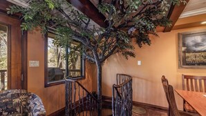 A room with a wooden staircase, a dining table, and chairs. - Disney Imagineer-Built Cabin, Pet Friendly, Fire Pit, Walk to Town Trails (Big Bear Lake)