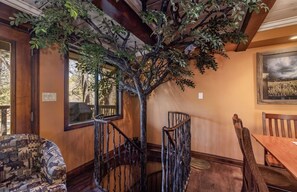 A room with a wooden staircase, a dining table, and chairs. - Disney Imagineer-Built Cabin | Pet Friendly | Fire Pit | Walk to Town Trails (Big Bear Lake)