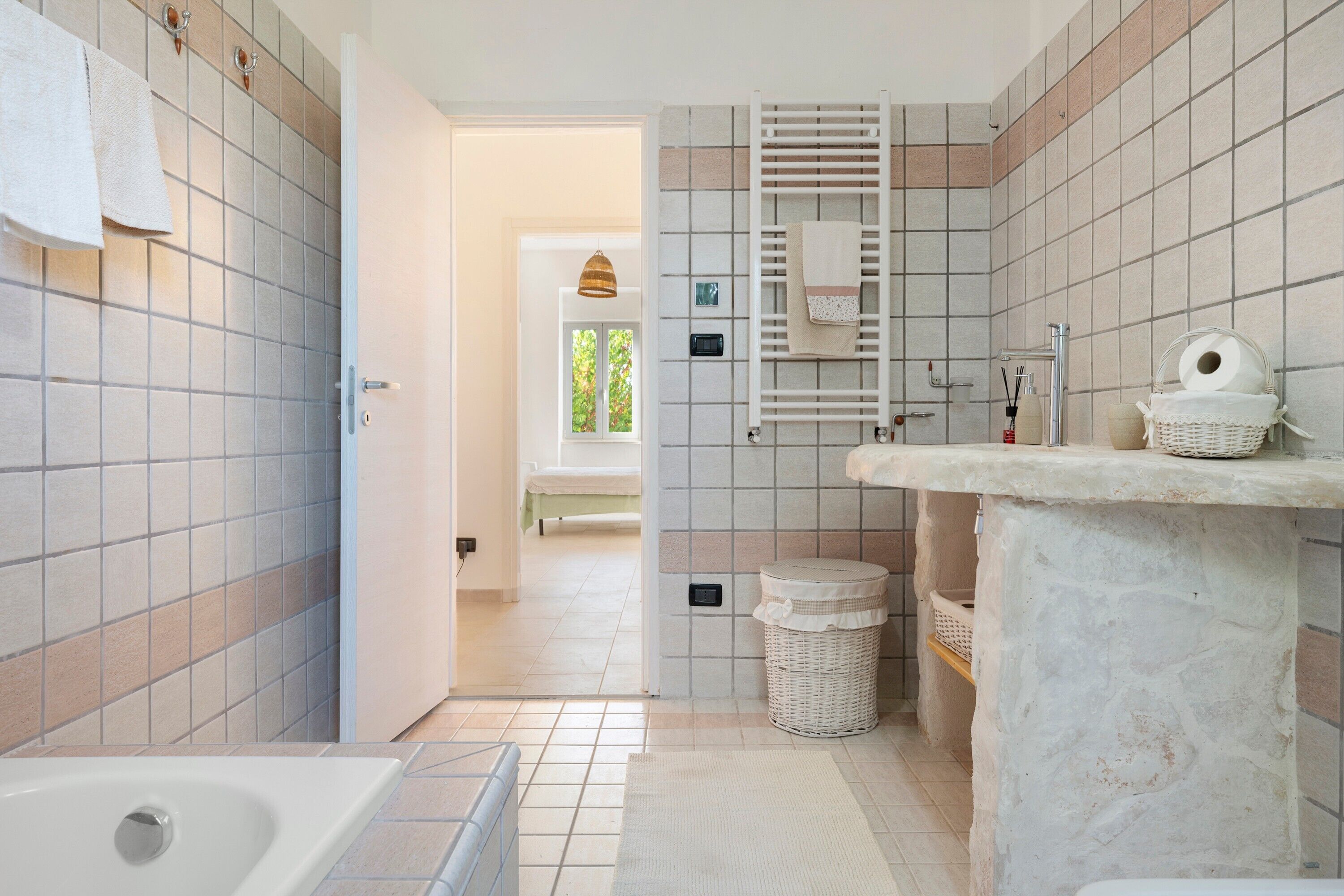 Ein Badezimmer mit Badewanne, Toilette, Waschbecken und Duschbereich. Ein Fenster bietet Blick auf Grünflächen.