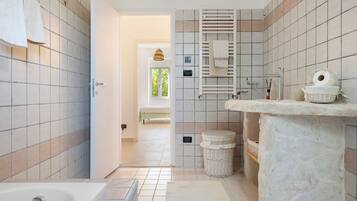 Ein Badezimmer mit Badewanne, Toilette, Waschbecken und Duschbereich. Ein Fenster bietet Blick auf Grünflächen.