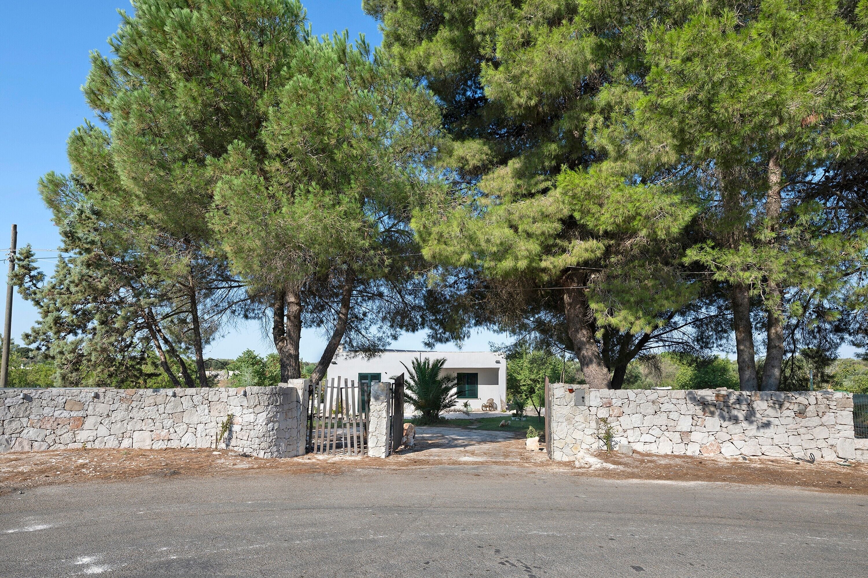 A stone wall with a gate leading to a building with a white facade and green shutters.