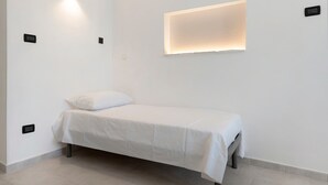 Ein schlicht eingerichteter Raum mit einem Einzelbett, einer Wandleuchte und einer Deckenleuchte.