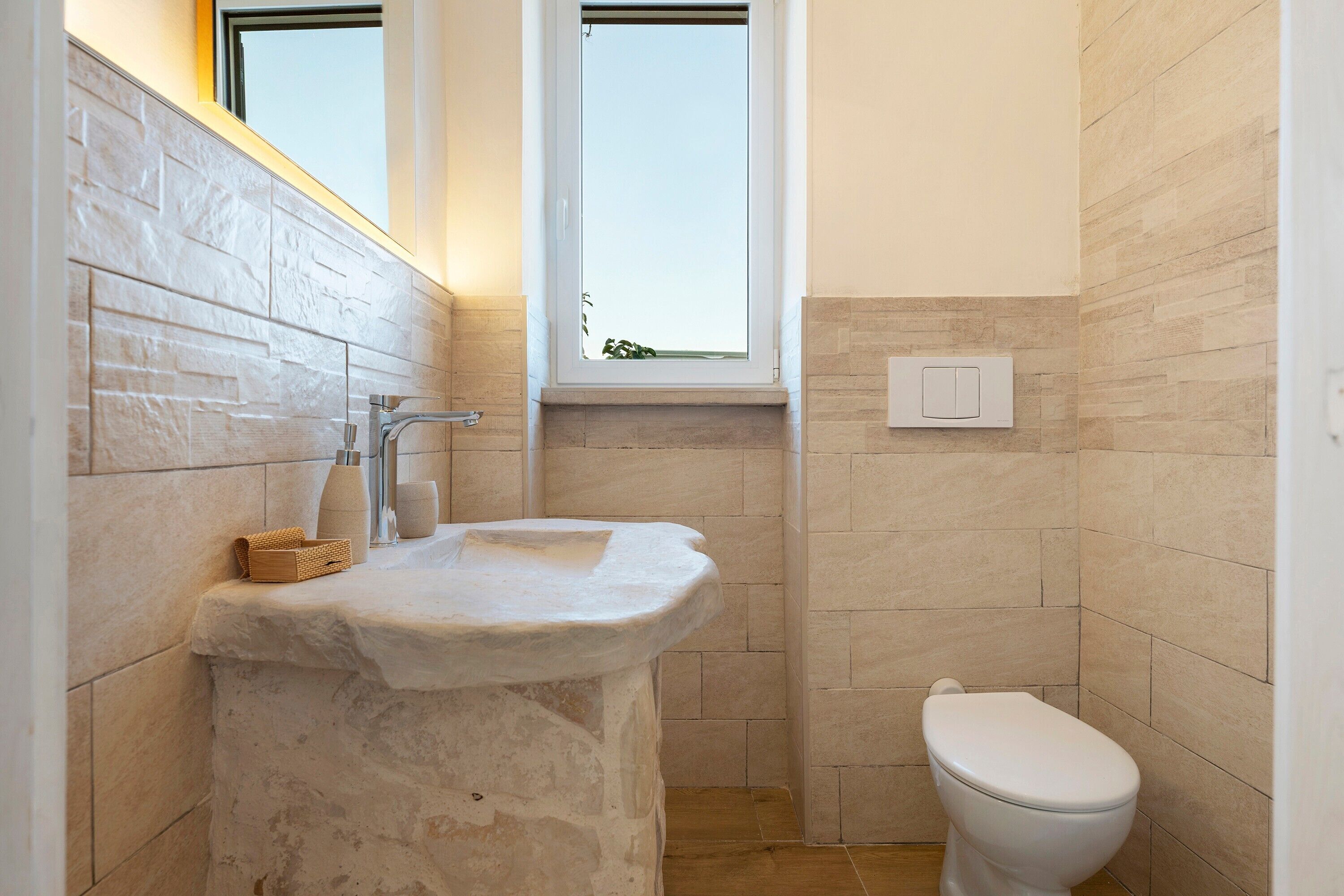 Une salle de bain avec un lavabo en pierre, des toilettes et une fenêtre située au-dessus du lavabo.