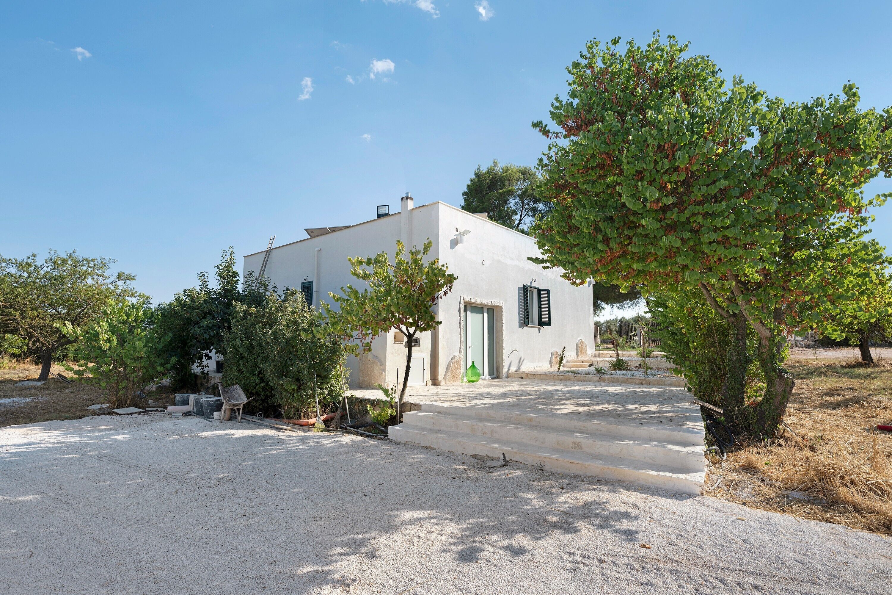 A white building with a door and windows, surrounded by gravel and trees.