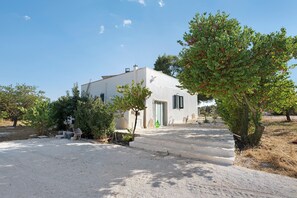 A white building with a door and windows, surrounded by gravel and trees.