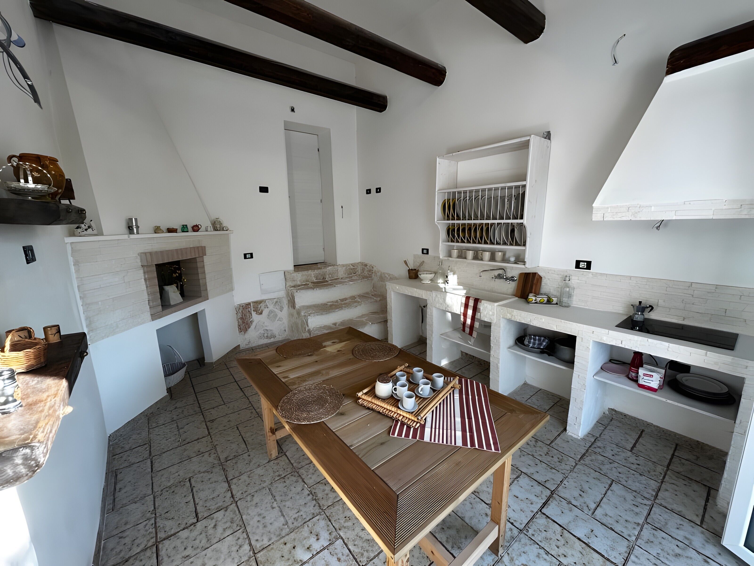 Una cucina moderna con camino in pietra, tavolo di legno e mobili bianchi.