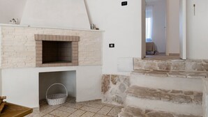 Ein Zimmer mit Kamin aus Backsteinen, einem Korb, einem Holztisch und einer Steintreppe.