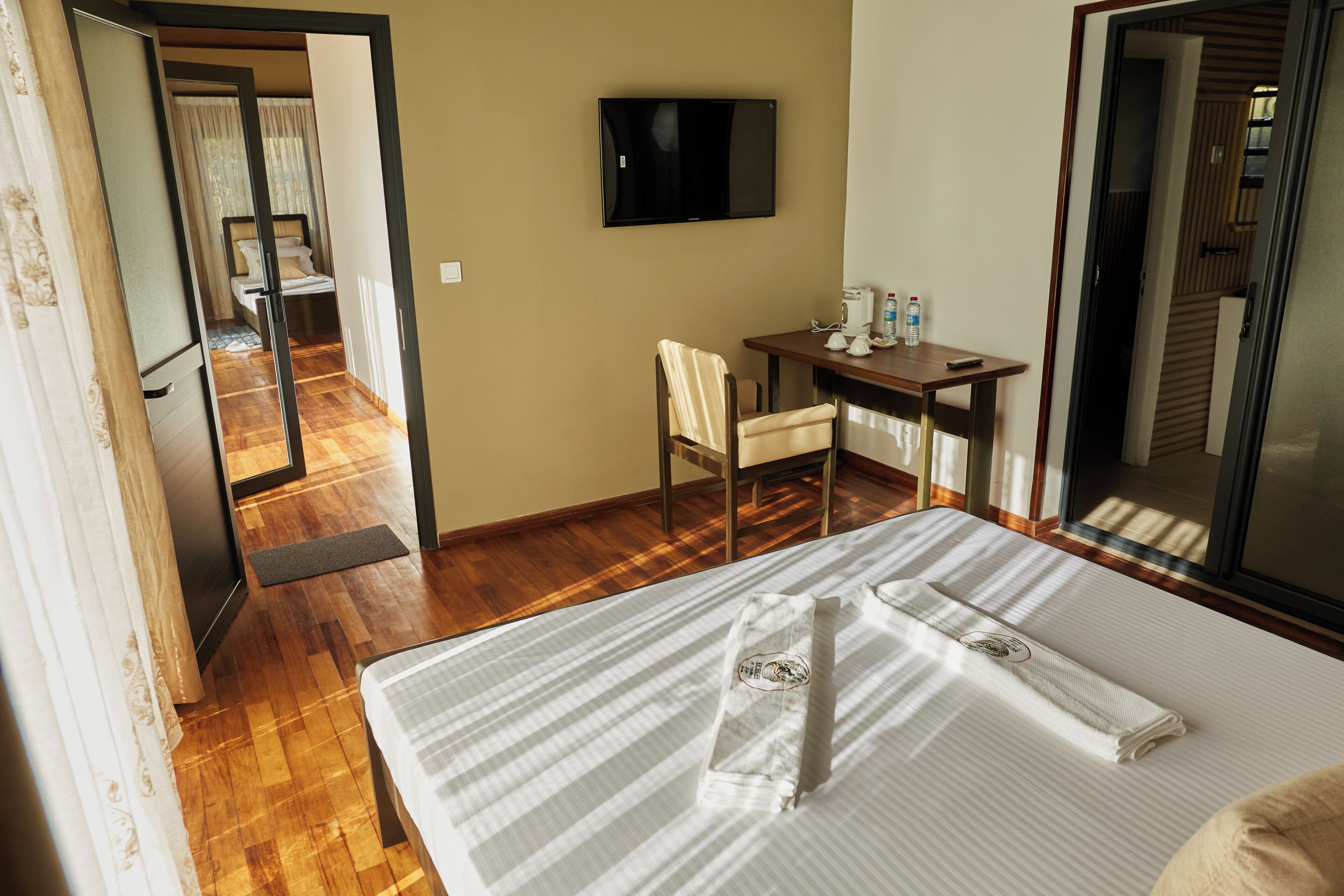 Quarto de hotel com cama, escrivaninha, cadeira, televisão e vista para o corredor.
