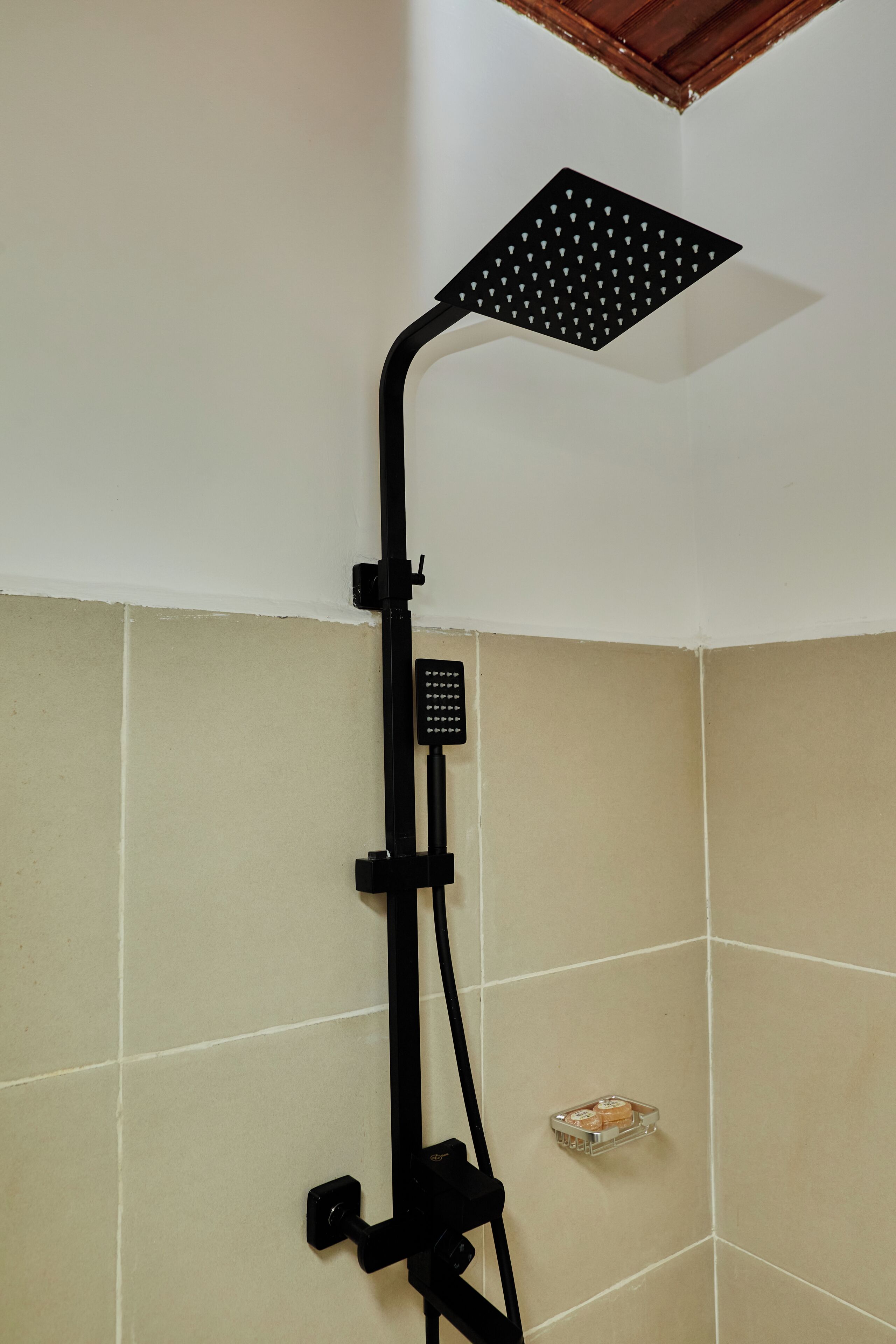 A shower with a black handheld showerhead and a wall-mounted control panel.