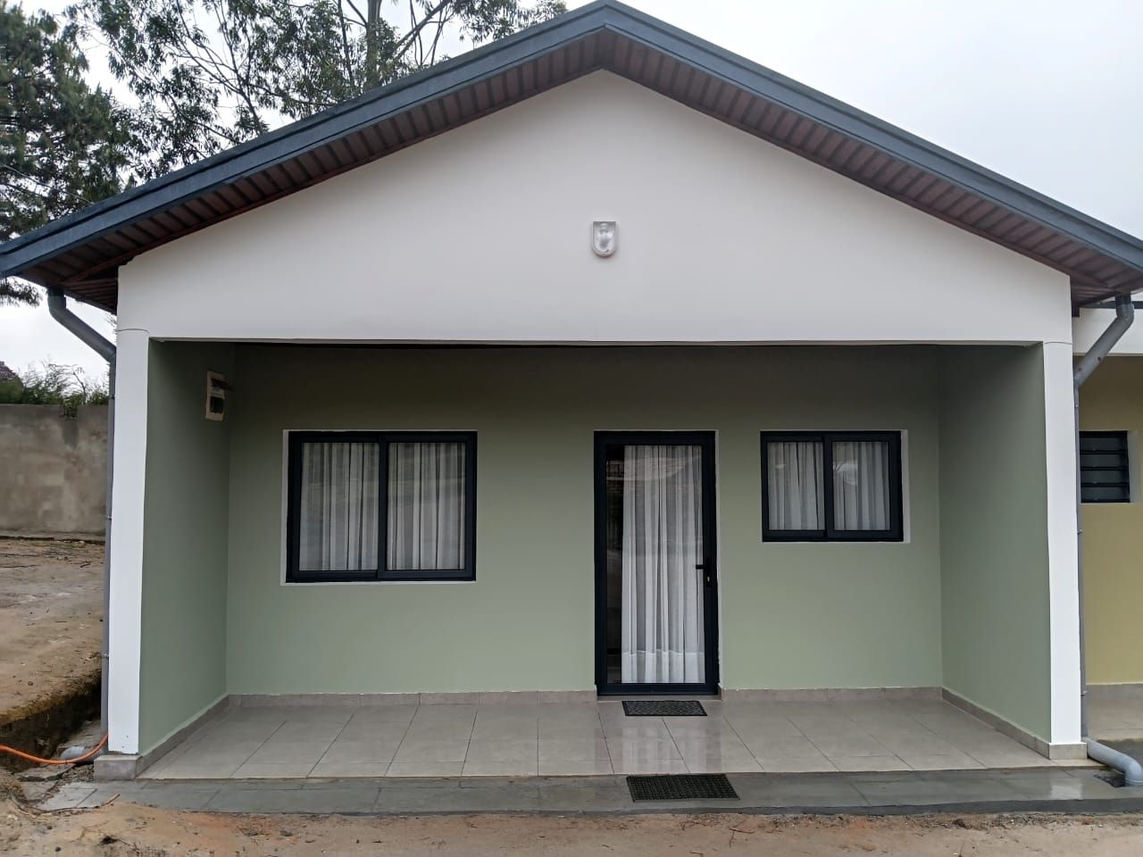 A single-story building with a flat roof, a front door, and two windows with curtains.