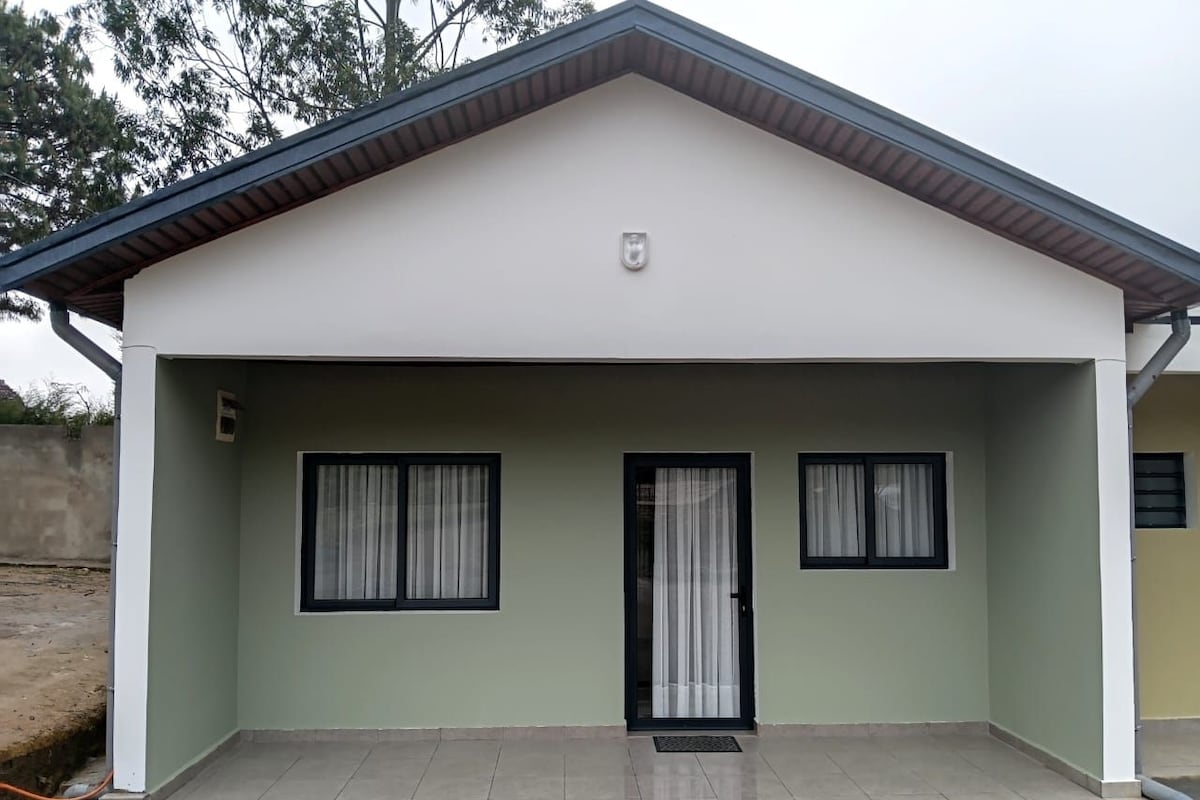 A single-story building with a flat roof, a front door, and two windows with curtains.