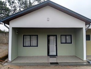 A single-story building with a flat roof, a front door, and two windows with curtains. - Echoes of the forest (Andasibe)